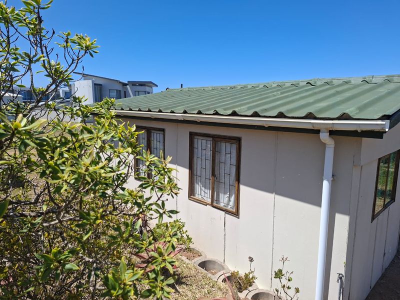Rear exterior view of the property featuring corrugated metal roofing, security-barred windows, and functional drainage systems.