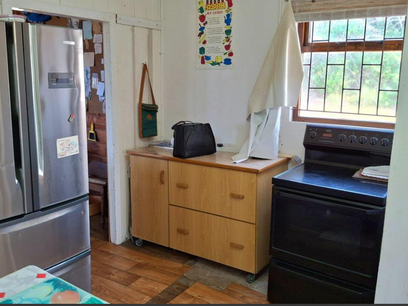 A compact kitchen area featuring timber cabinetry, a freestanding stove, and security bars on the window, with wood-look laminate flooring throughout.