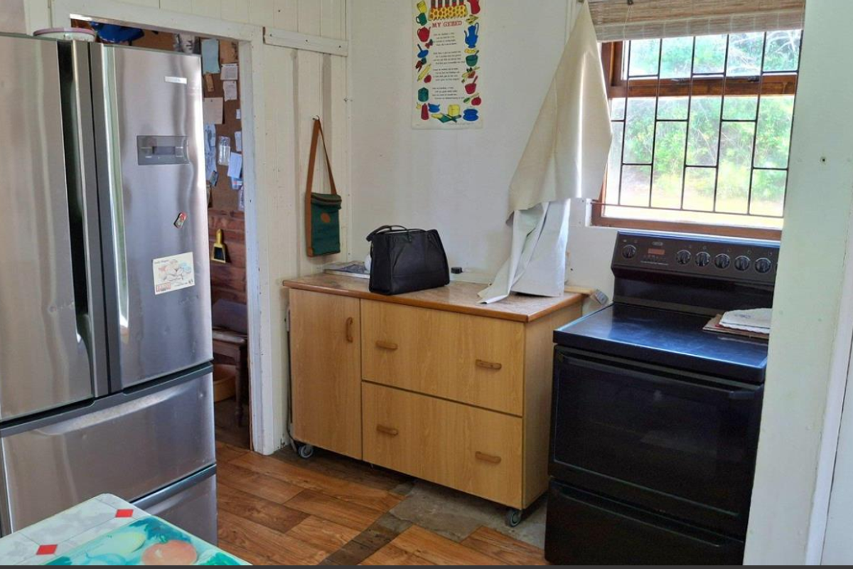 A compact kitchen area featuring timber cabinetry, a freestanding stove, and security bars on the window, with wood-look laminate flooring throughout.