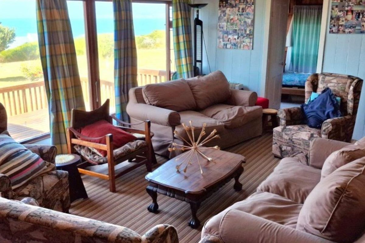 A living room featuring timber wall paneling and large sliding glass doors that open onto an outdoor timber deck with coastal views.
