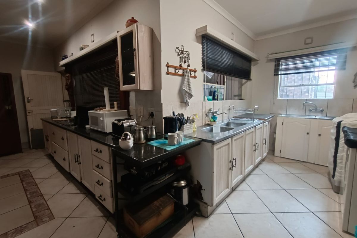 A dated kitchen featuring L-shaped cabinetry, dark stone countertops, double stainless steel sink, and tiled flooring.