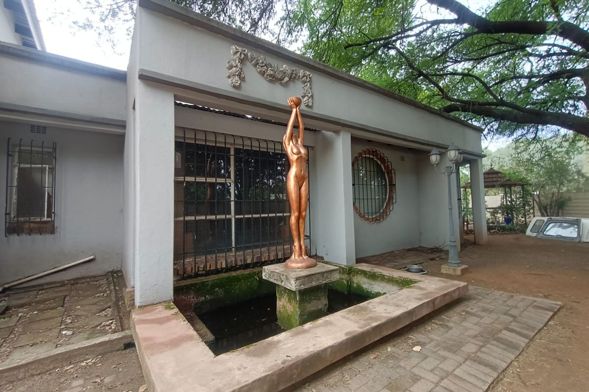 Rear exterior view featuring a decorative fountain with a central statue, paved patio area, and established garden surroundings.