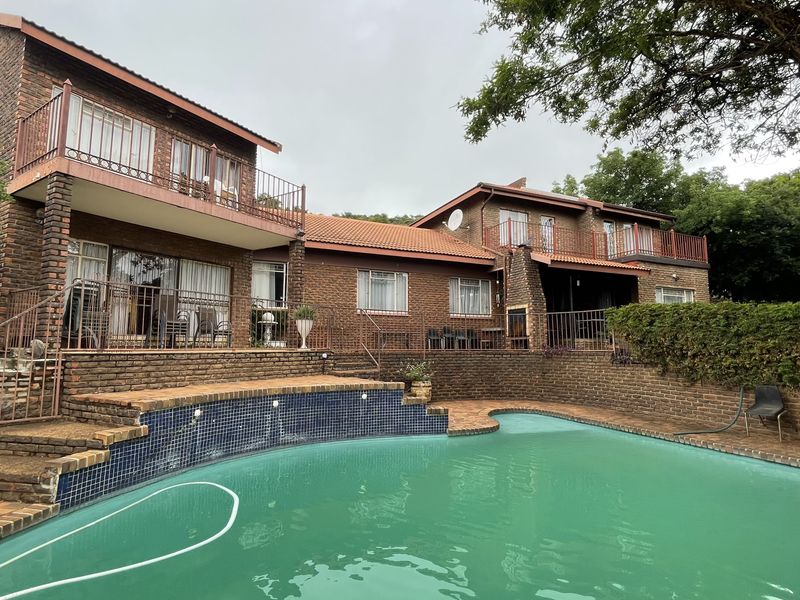 Rear view of a multi-story brick house featuring a swimming pool, upper-level balconies, and an outdoor fireplace area.