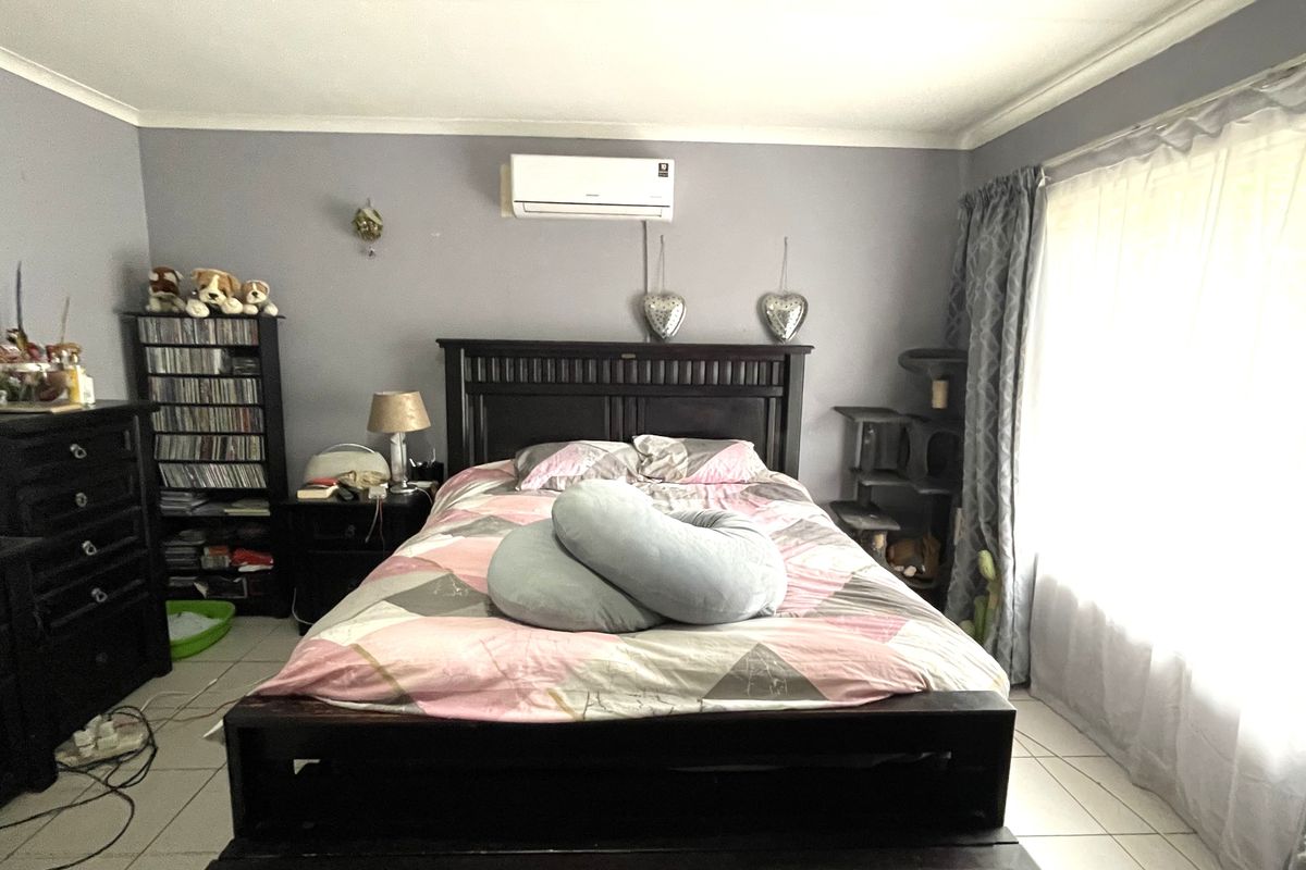 A bedroom featuring tiled flooring and a wall-mounted split-system air conditioner, offering a functional space with natural light from the window.