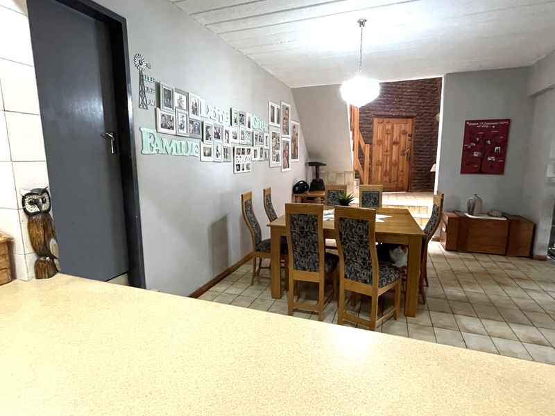 An open-plan dining area featuring tiled flooring, a central pendant light, and access to a staircase and wooden door.