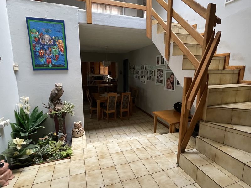 Open plan living area featuring a central wooden staircase with balustrade and tiled flooring, leading through to a dining space and kitchen.