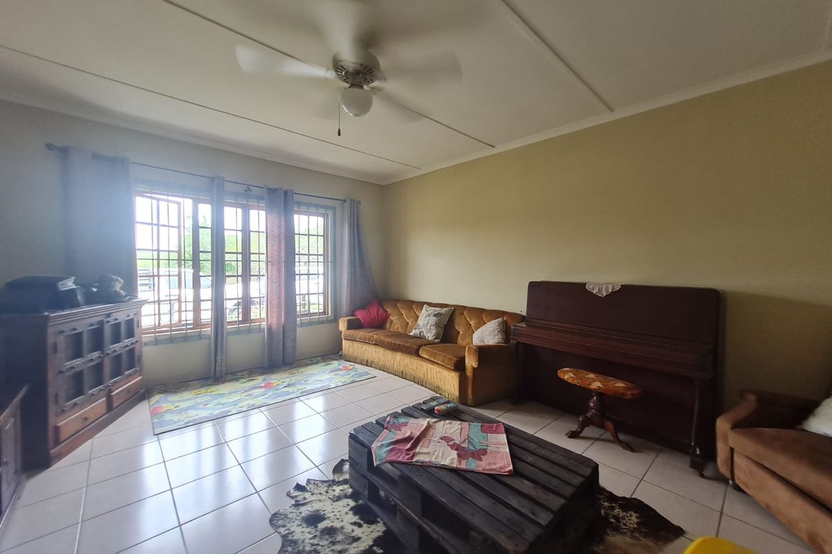A spacious living room featuring tiled flooring, a ceiling fan, and large windows with security bars, offering a functional and comfortable living space.