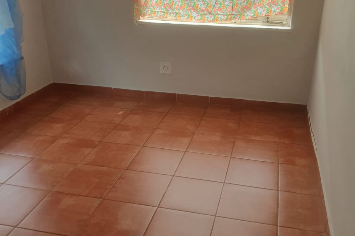 A vacant bedroom featuring terracotta-style floor tiles, a single window, and a wall-mounted electrical outlet.