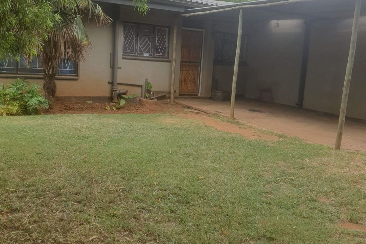 Rear view of the property featuring a paved patio area, lawn, and exterior access door.