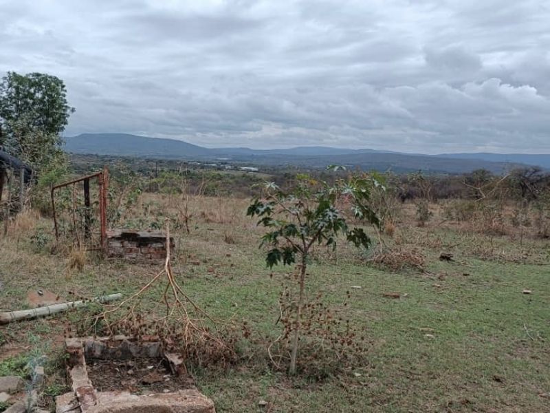 Expansive rural landscape view featuring natural terrain and distant mountain ranges, with remnants of old brick and metal structures in the foreground.