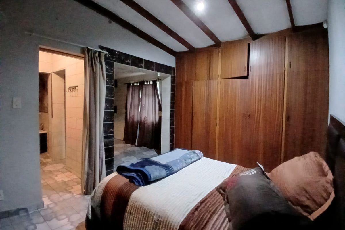 Bedroom featuring built-in wooden cupboards, exposed ceiling beams, and an adjoining en-suite bathroom with tiled flooring.