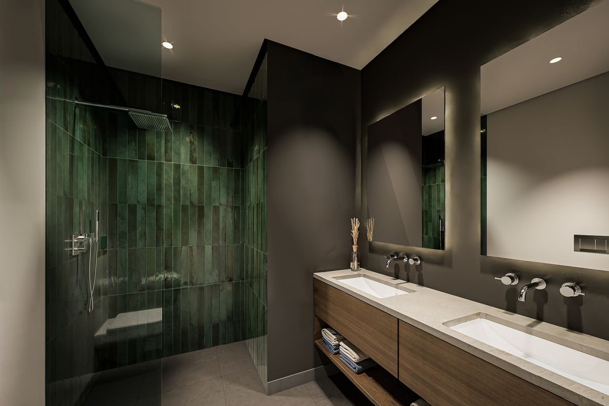 Modern bathroom featuring a double vanity with integrated sinks, wall-mounted faucets, and a spacious walk-in shower with dark green tiled walls.