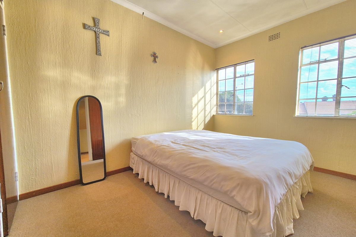A bedroom featuring textured walls, carpeted flooring, and two windows with metal frames, providing natural light.