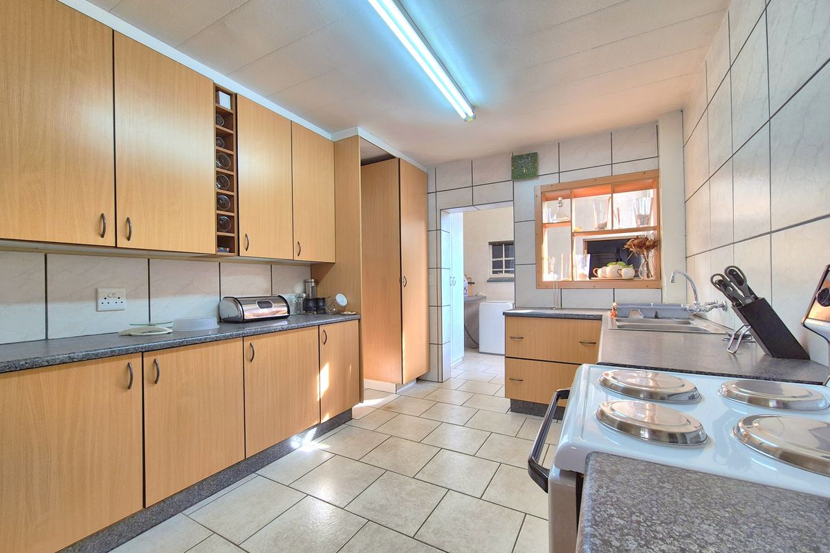 A functional kitchen featuring light wood cabinetry, laminate countertops, tiled flooring, and a built-in stove, with an adjacent scullery area visible.