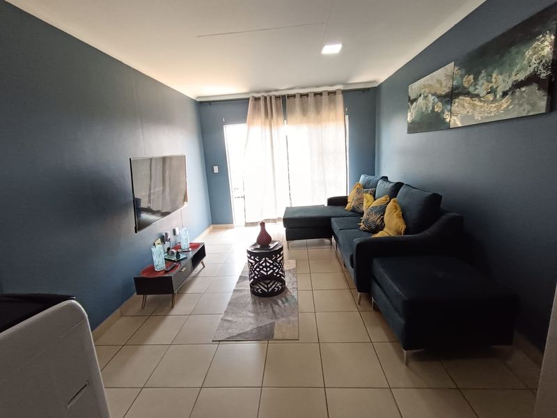 A well-maintained living room featuring neutral tiled flooring, recessed ceiling lighting, and a sliding glass door providing access to the exterior.