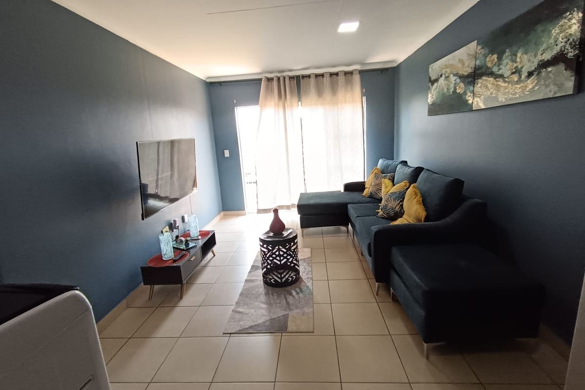 A well-maintained living room featuring neutral tiled flooring, recessed ceiling lighting, and a sliding glass door providing access to the exterior.