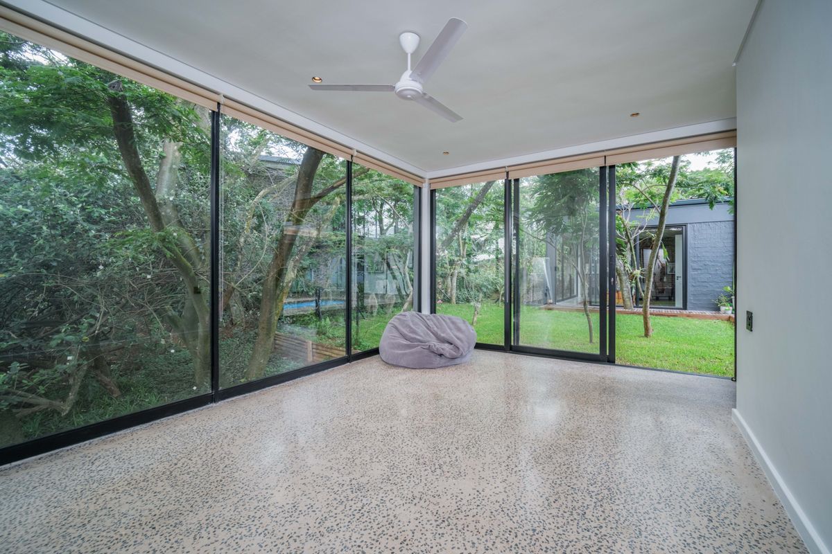 Bright living space featuring floor-to-ceiling glass sliding doors, polished concrete flooring, and a ceiling fan, offering seamless indoor-outdoor flow to the garden.