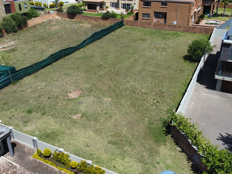 An aerial view of a vacant residential plot featuring perimeter walling and established boundary fencing, situated within a developed residential estate.