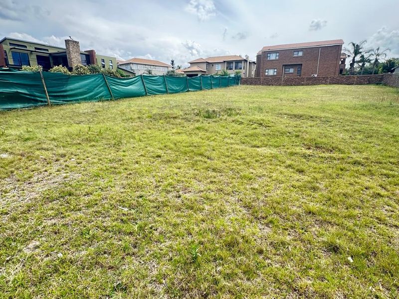 A vacant residential plot featuring a grass lawn and perimeter fencing, situated in a developed neighborhood.