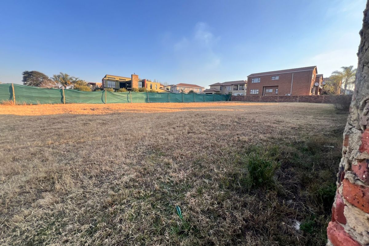 A vacant residential plot featuring dry grass and perimeter fencing with green shade cloth screening, situated in a developed neighborhood.