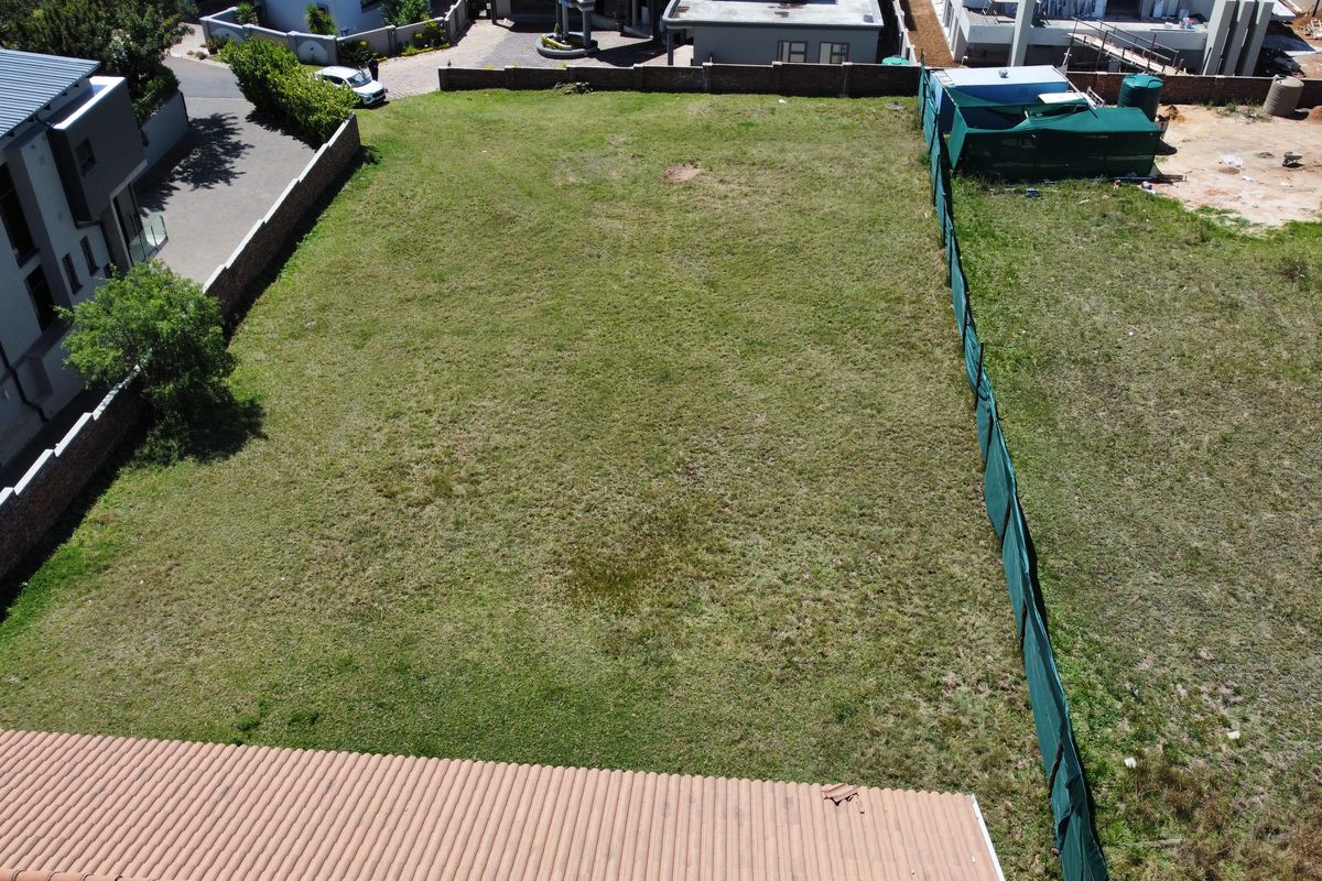 An aerial view of a vacant residential plot featuring grass coverage and perimeter boundary walls with green shade cloth fencing.