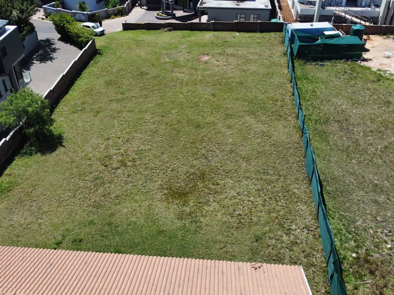 An aerial view of a vacant residential plot featuring grass coverage and perimeter boundary walls with green shade cloth fencing.