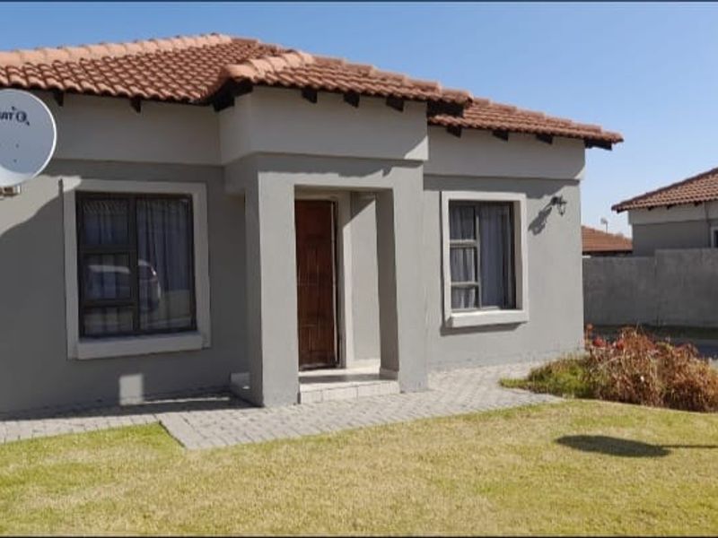 Front elevation of a townhouse featuring a tiled roof, paved driveway, and a small front garden area.