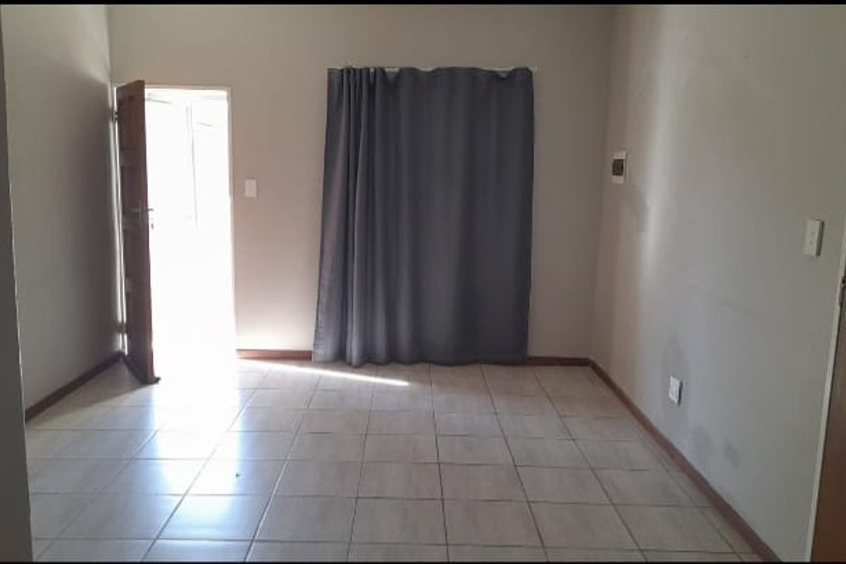 An empty living room featuring tiled flooring, neutral walls, and direct access to an outdoor area through a doorway.