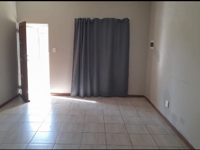 An empty living room featuring tiled flooring, neutral walls, and direct access to an outdoor area through a doorway.