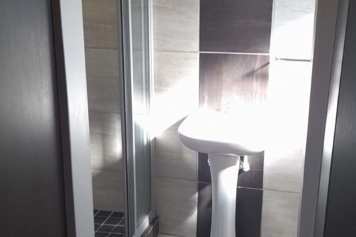 A compact bathroom featuring a pedestal basin and a glass-enclosed shower with modern two-tone tiled finishes.