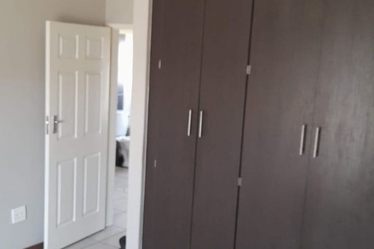 A clean, empty bedroom featuring neutral wall tones, tiled flooring, and dark wood-finish built-in cupboards.