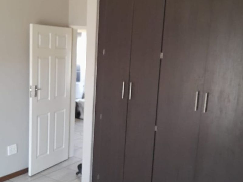 A clean, empty bedroom featuring neutral wall tones, tiled flooring, and dark wood-finish built-in cupboards.