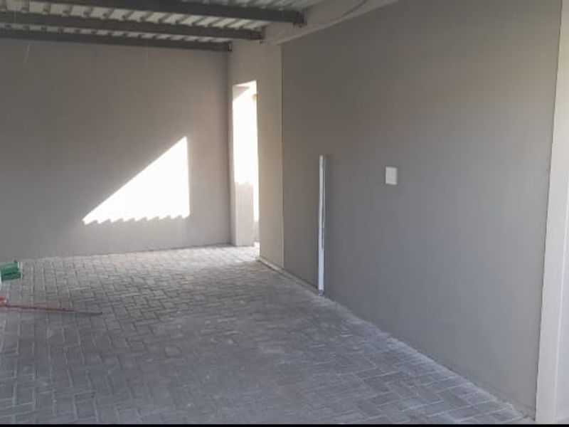 A clean, empty garage space featuring paved flooring, exposed ceiling beams, and a solid door, providing a versatile area for parking or storage.