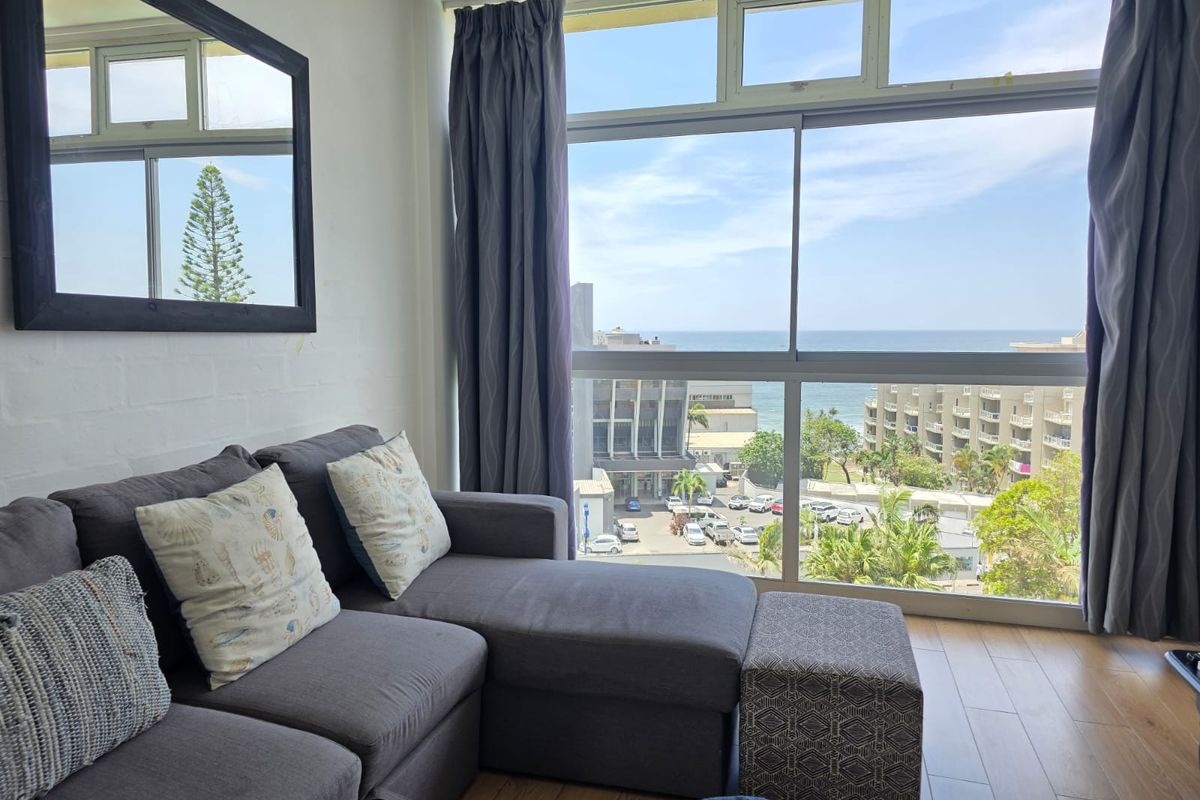 A bright living room featuring large windows with expansive ocean and coastal views, complemented by wood-look flooring.