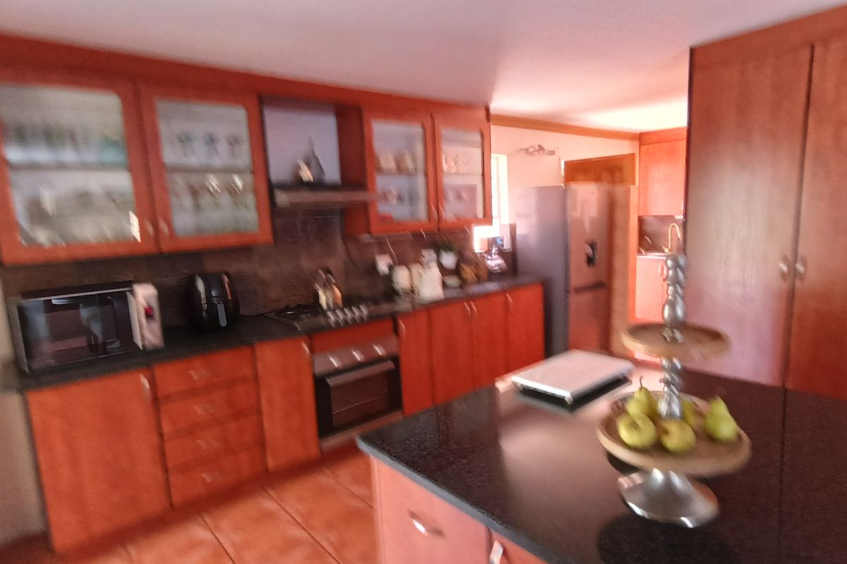 A functional kitchen featuring warm-toned wooden cabinetry, a central island with a dark countertop, and integrated cooking appliances.