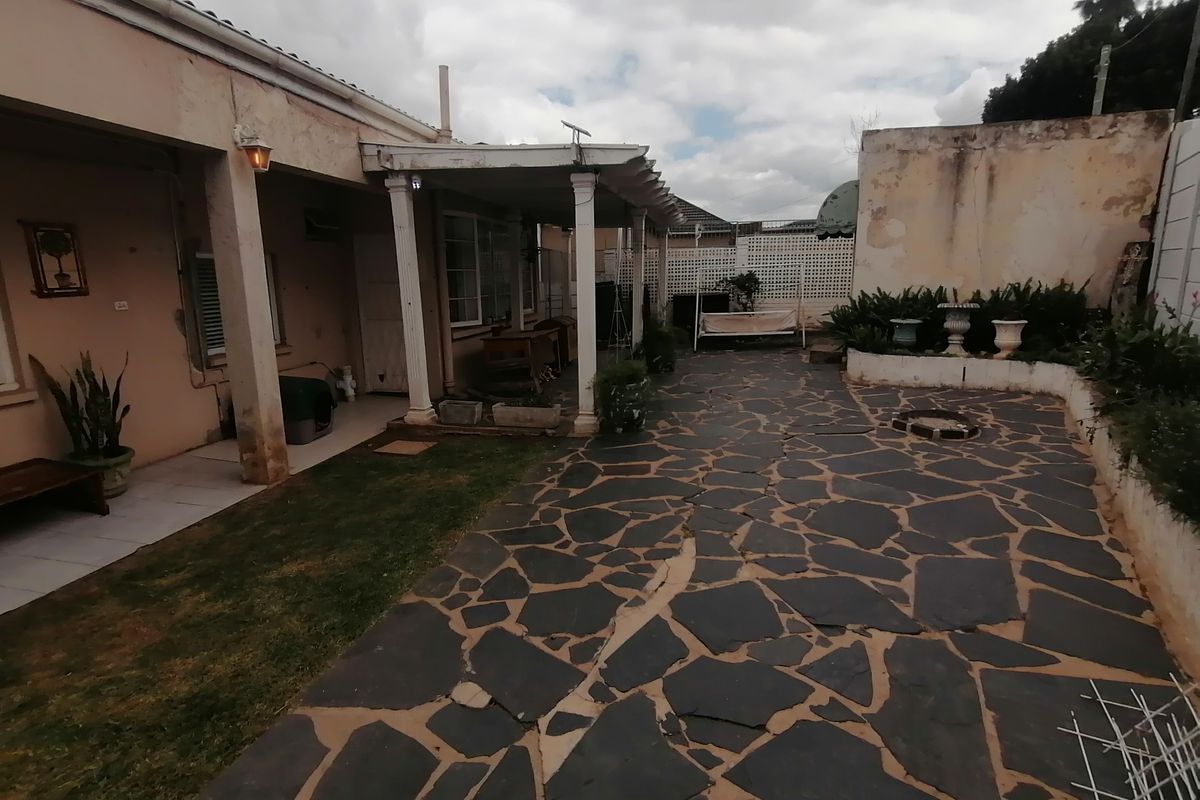 Rear courtyard featuring a covered patio area, paved flooring, and a raised garden bed against a boundary wall.