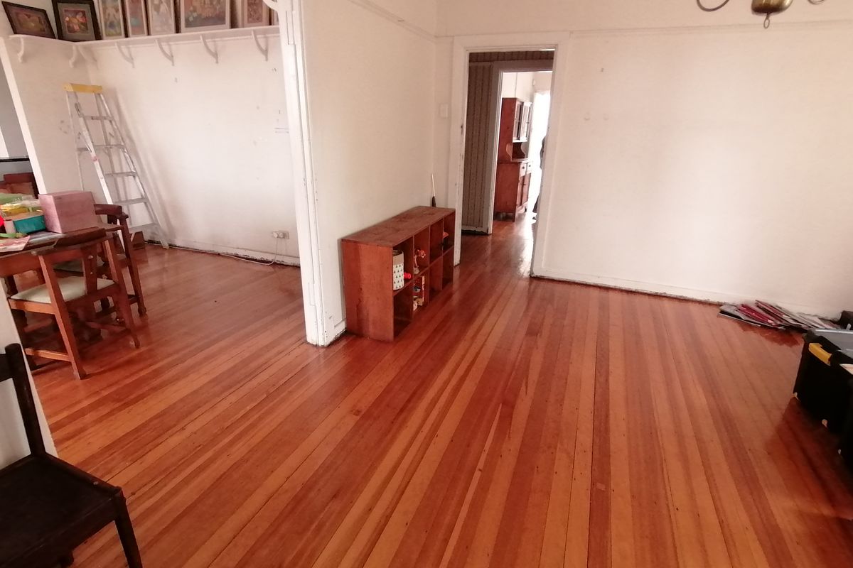 A living area featuring polished timber flooring, high ceilings with picture rails, and an open-plan layout connecting to adjacent rooms.