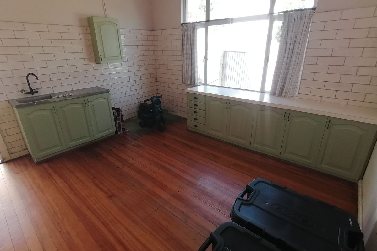 A functional kitchen area featuring sage green cabinetry, white subway tile splashbacks, and polished timber flooring with ample natural light.