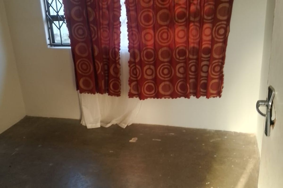 A small, unfinished bedroom featuring a window with security bars and exposed concrete flooring, awaiting final floor finishes and interior updates.