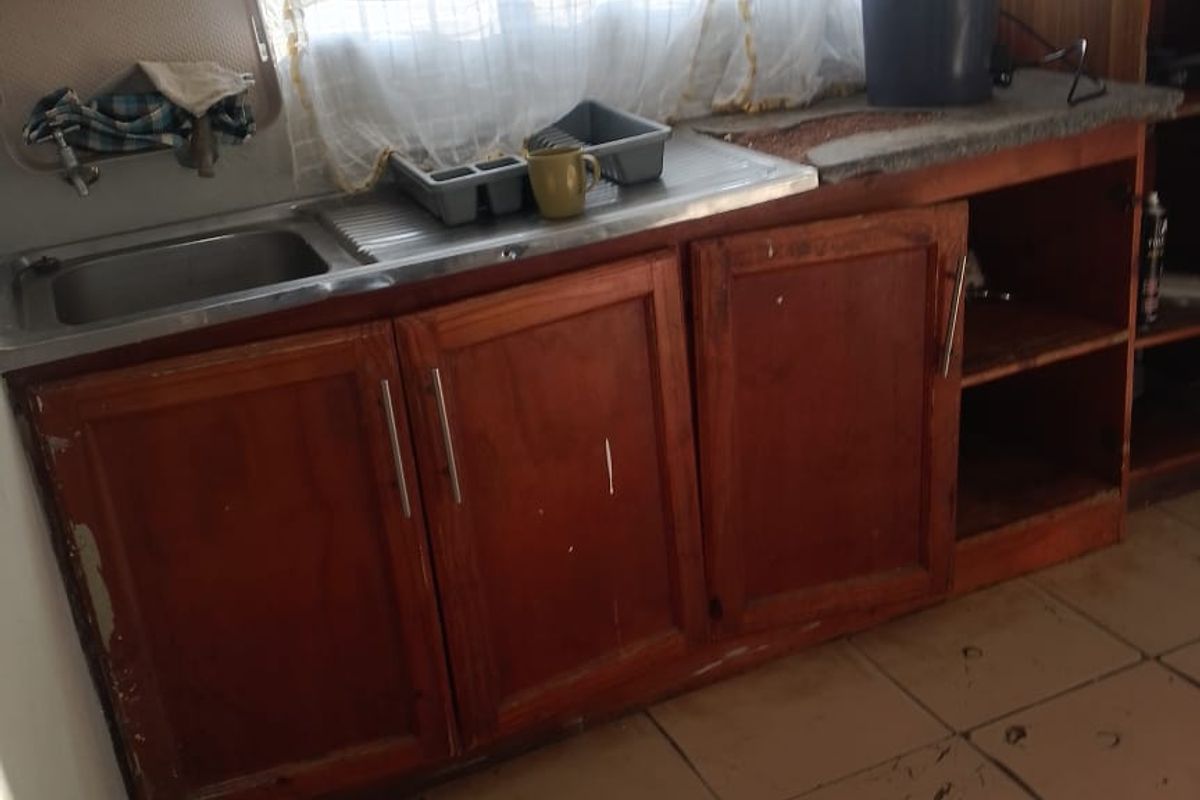 A dated kitchen area featuring wooden cabinetry, a stainless steel sink, and tiled flooring, requiring cosmetic updates and maintenance.