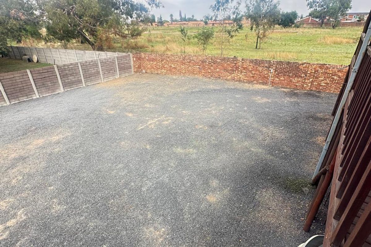 A spacious, open-plan vacant residential plot featuring a gravel surface, enclosed by brick and precast concrete boundary walls with surrounding landscape views.
