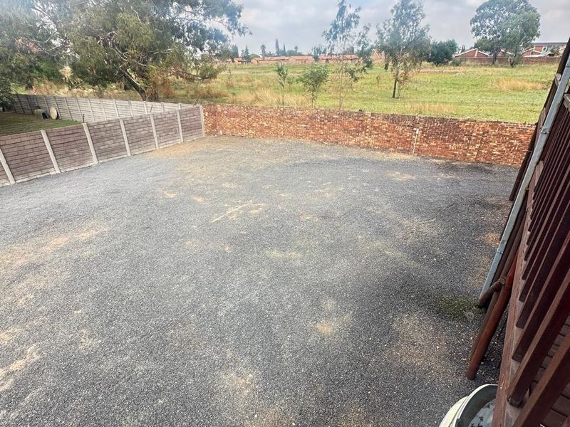 A spacious, open-plan vacant residential plot featuring a gravel surface, enclosed by brick and precast concrete boundary walls with surrounding landscape views.