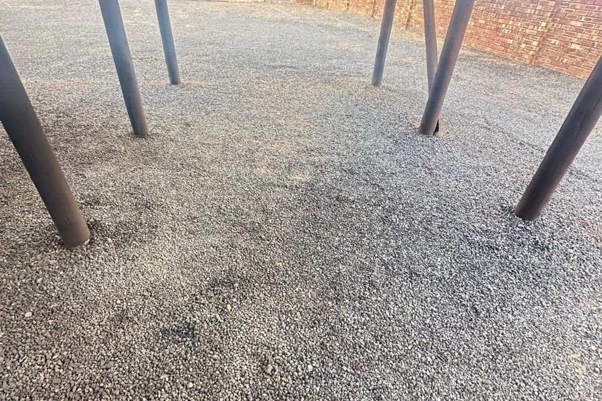 A view of a vacant residential plot featuring a gravel surface, perimeter brick boundary walls, and structural support poles.