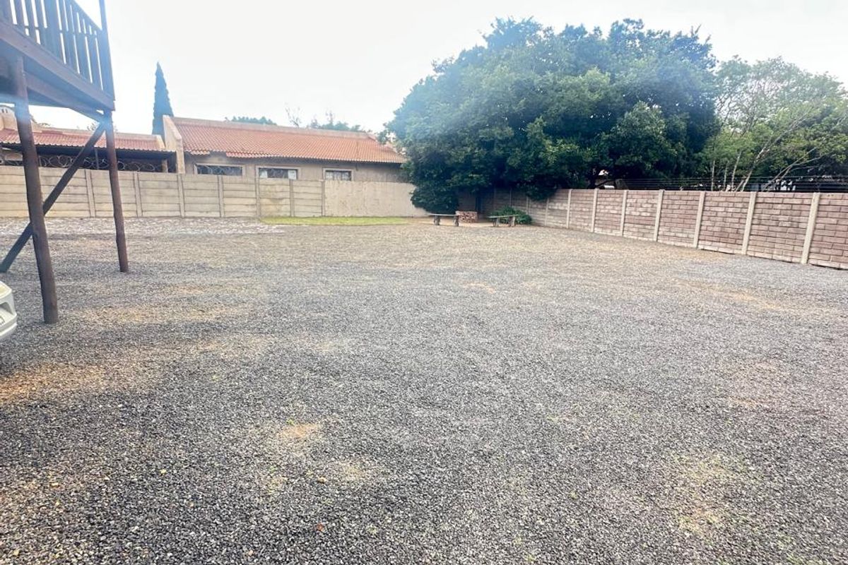 A spacious, level backyard area featuring a gravel surface, enclosed by perimeter boundary walls, with a raised wooden deck structure visible on the left.