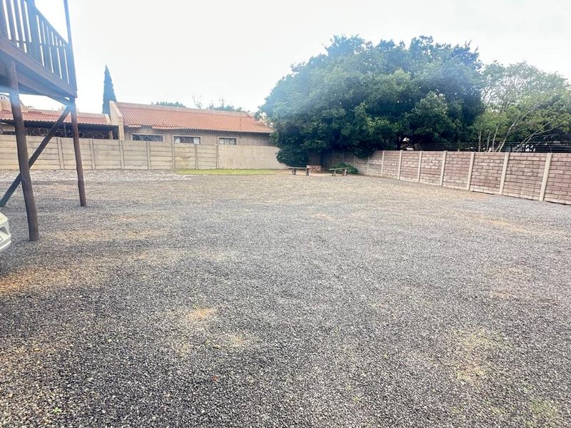 A spacious, level backyard area featuring a gravel surface, enclosed by perimeter boundary walls, with a raised wooden deck structure visible on the left.
