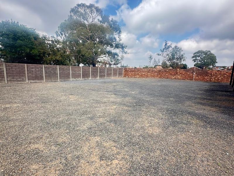 A spacious, level vacant residential plot featuring a gravel surface and enclosed by perimeter brick and precast concrete boundary walls.