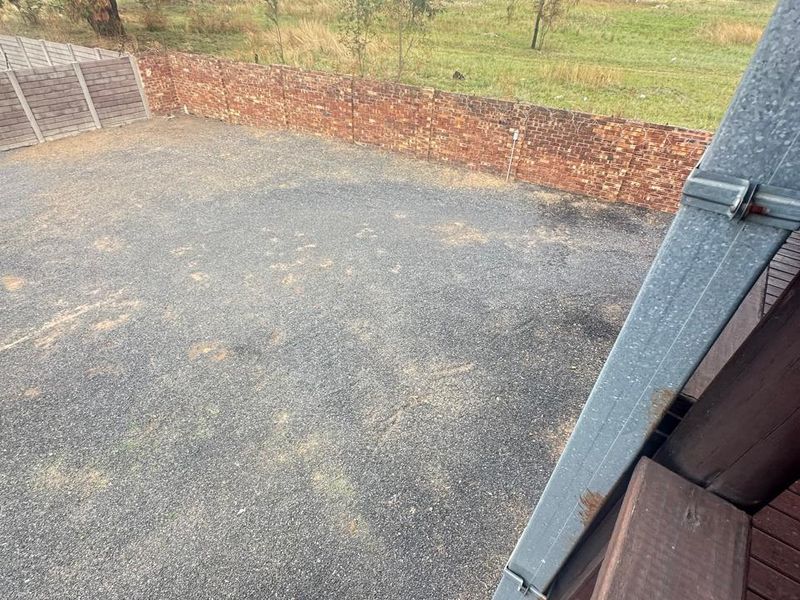 An elevated view of a vacant residential plot featuring a gravel surface, enclosed by brick and precast concrete boundary walls.
