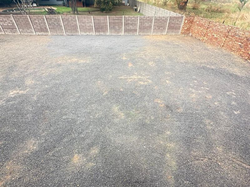 A vacant residential plot featuring a gravel-covered surface, enclosed by a combination of precast concrete and brick boundary walls.