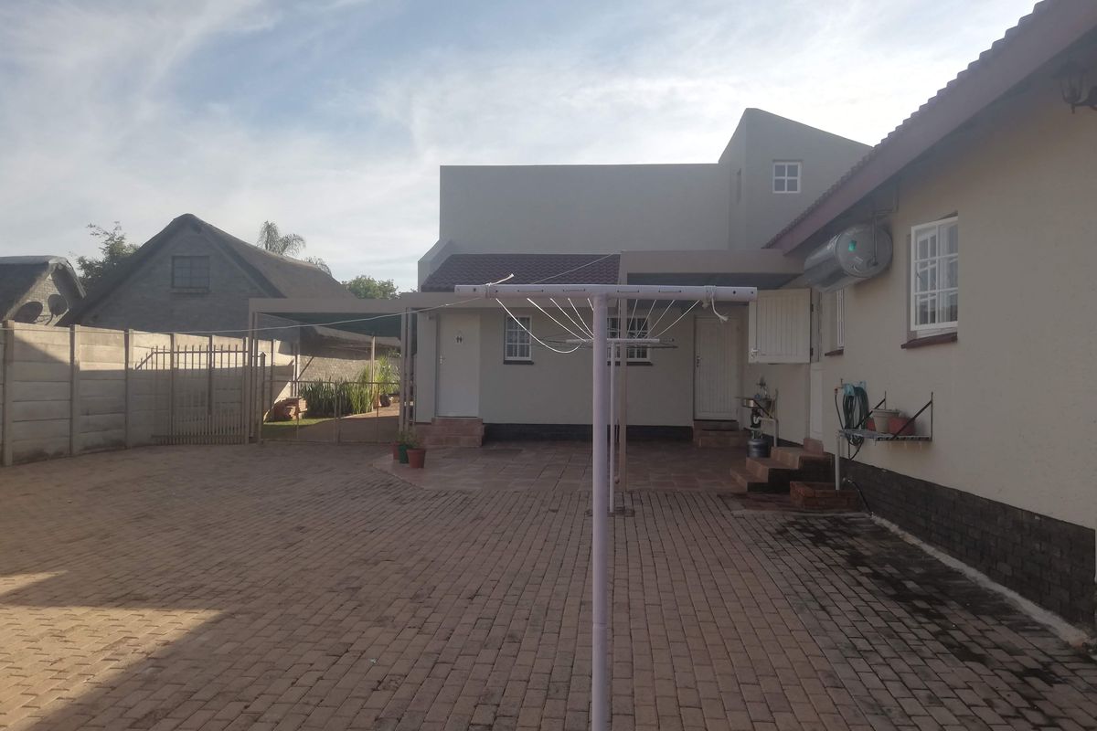 Rear exterior view of the property featuring a paved courtyard, covered patio area, and exterior wall-mounted geyser.