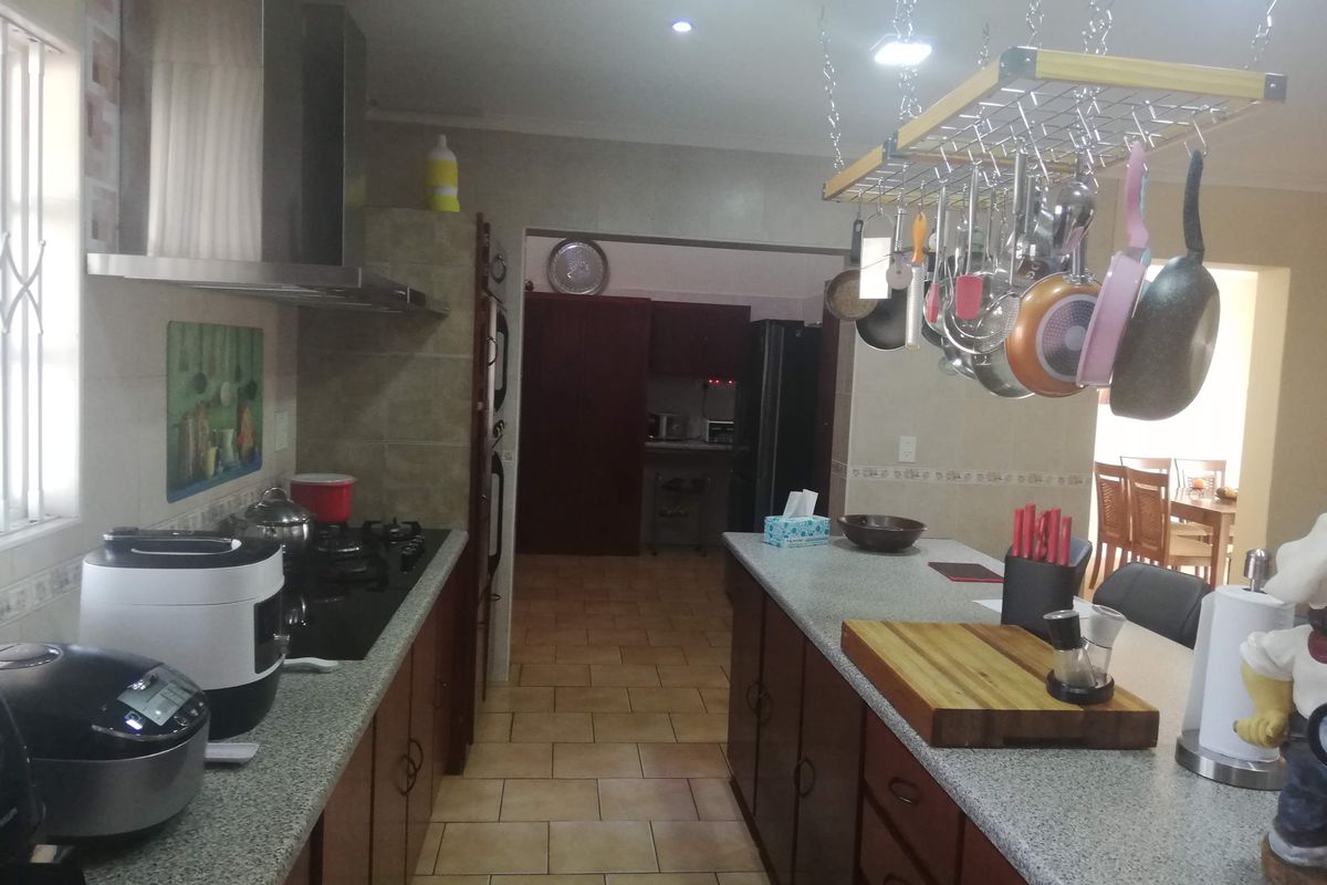 A functional kitchen featuring dark wood cabinetry, granite countertops, a gas hob with extractor fan, and a central island with overhead pot rack.